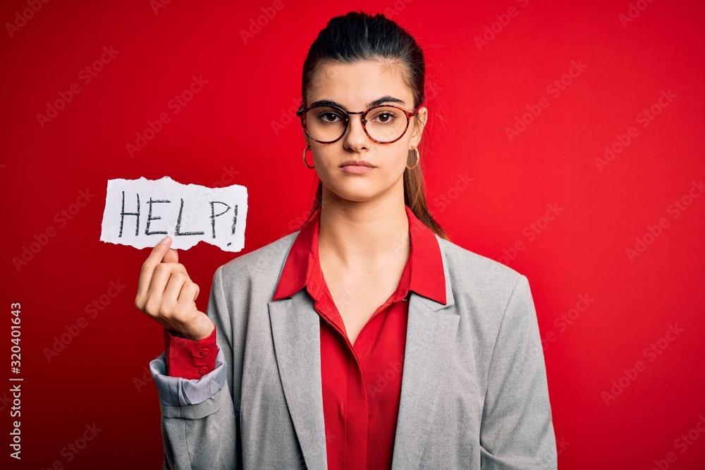 Young beautiful brunette businesswoman with problems holding paper with help message with a confident expression on smart face thinking serious Young beautiful brunette businesswoman with problems holding paper with help message with a confident expression on smart face thinking serious