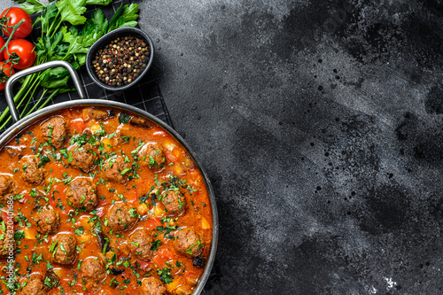 Beef meatballs with tomato sauce and vegetables in a pan. Black background. Top view. Space for text