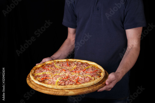 service and people concept - delivery man with pizza. Waiter holds a plate of tasty food. Italian cuisine in restaurant. Delicious pizza. Large meat pizza with bacon, sausage, salami, pepperoni and ol