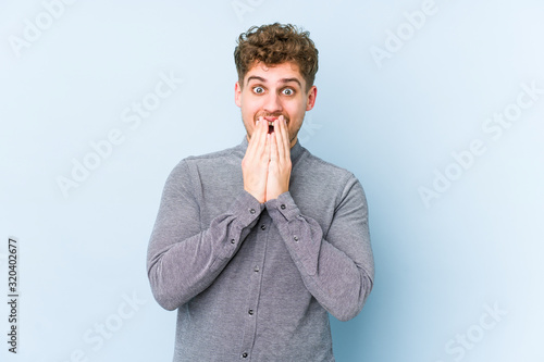 Young blond curly hair caucasian man isolated shocked  covering mouth with hands  anxious to discover something new.