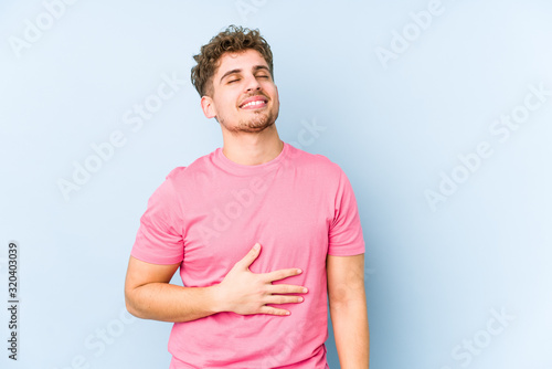 Young blond curly hair caucasian man isolated touches tummy, smiles gently, eating and satisfaction concept.