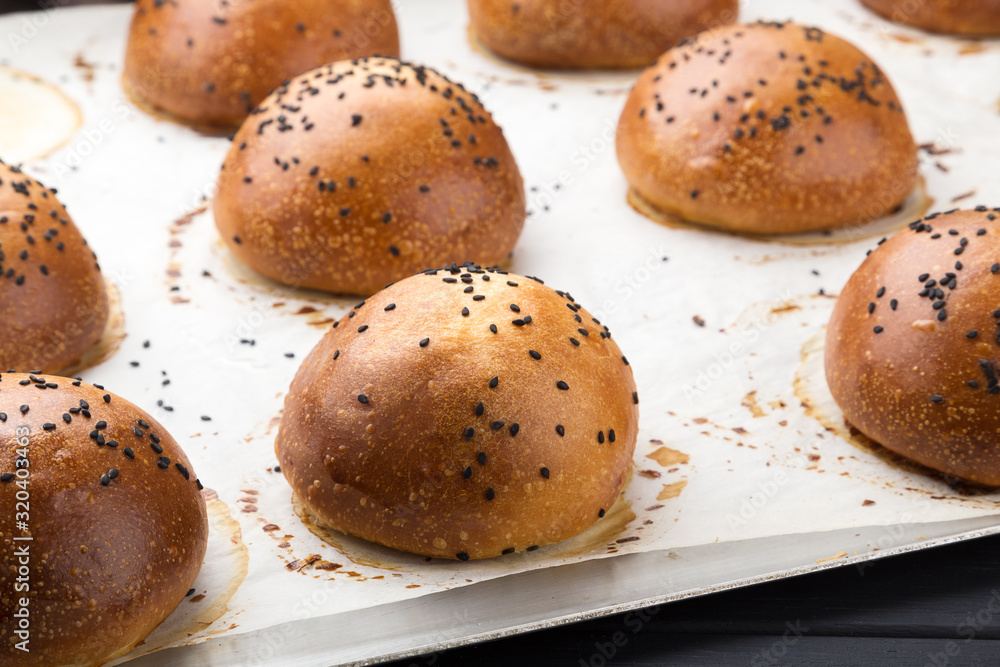 Delicious fresh round buns with sesame seeds on a board. Homemade whole wheat burger buns with sesame seeds on wooden background. Delicious fresh round buns with sesame seeds on a board. Homemade whole wheat burger buns with sesame seeds on wooden background.