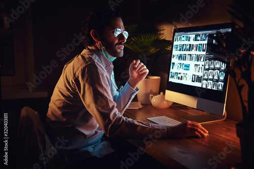 At the dark office young intern in glasses is working with x-ray images using computer.