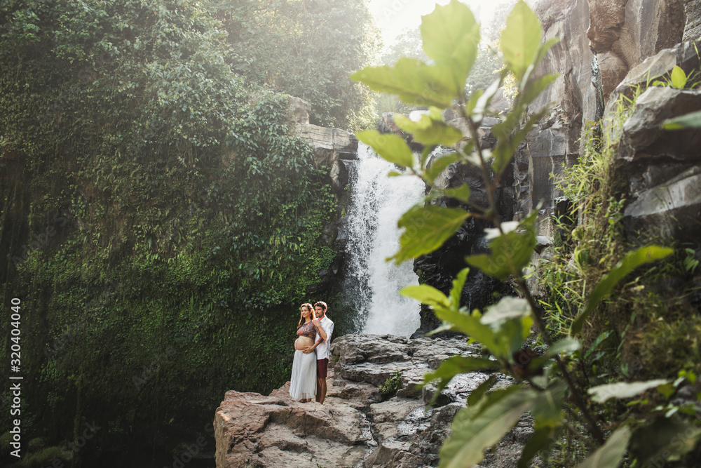 Φωτογραφία Young pregnant couple travel together with view of Tegenungan cascade waterfall in Bali