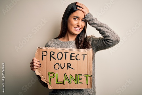 Young beautiful brunette activist woman protesting for protect our planet holding poster stressed with hand on head, shocked with shame and surprise face, angry and frustrated. Fear and upset © Krakenimages.com