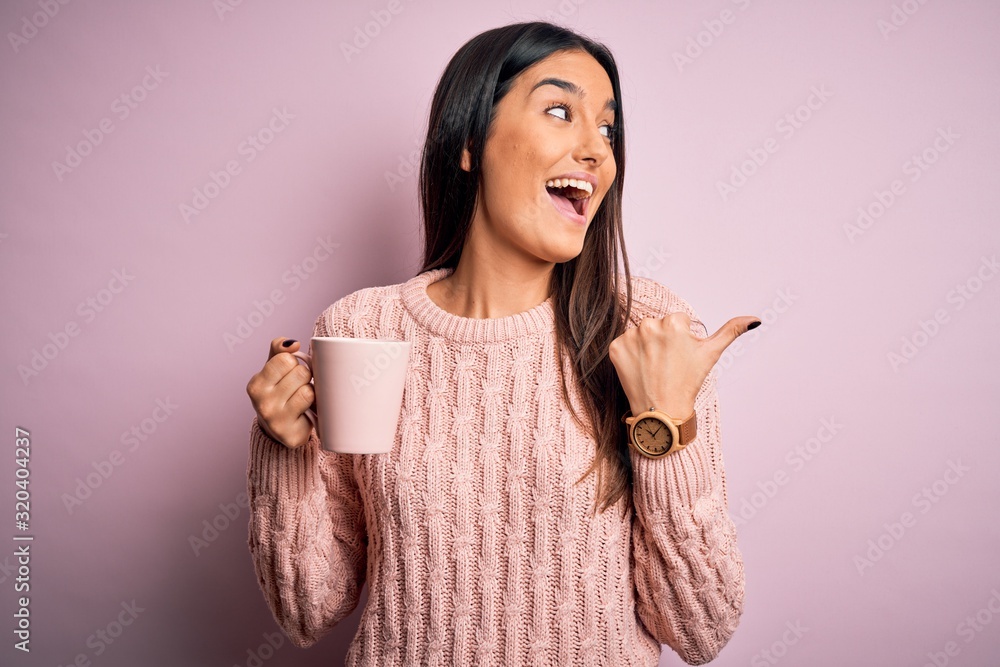 Young beautiful brunette woman drinking cup of coffee over isolated pink background pointing and showing with thumb up to the side with happy face smiling Young beautiful brunette woman drinking cup of coffee over isolated pink background pointing and showing with thumb up to the side with happy face smiling