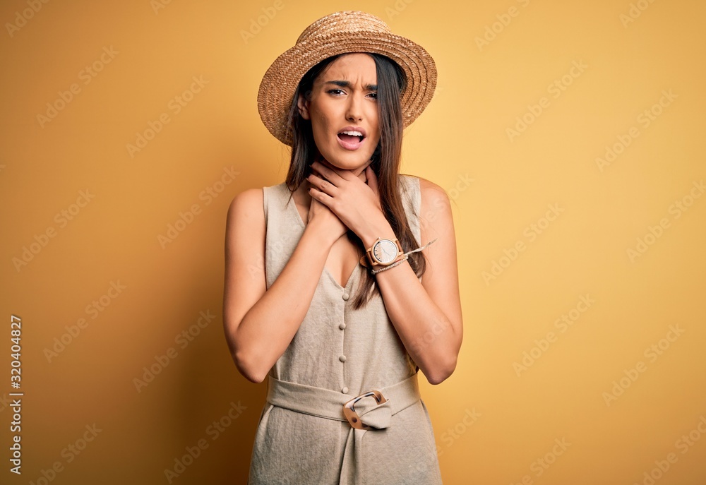 Young beautiful brunette woman on vacation wearing casual dress and hat shouting and suffocate because painful strangle. Health problem. Asphyxiate and suicide concept. Young beautiful brunette woman on vacation wearing casual dress and hat shouting and suffocate because painful strangle. Health problem. Asphyxiate and suicide concept.
