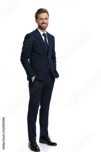 Fototapeta happy young businessman holding hands in pockets and smiling