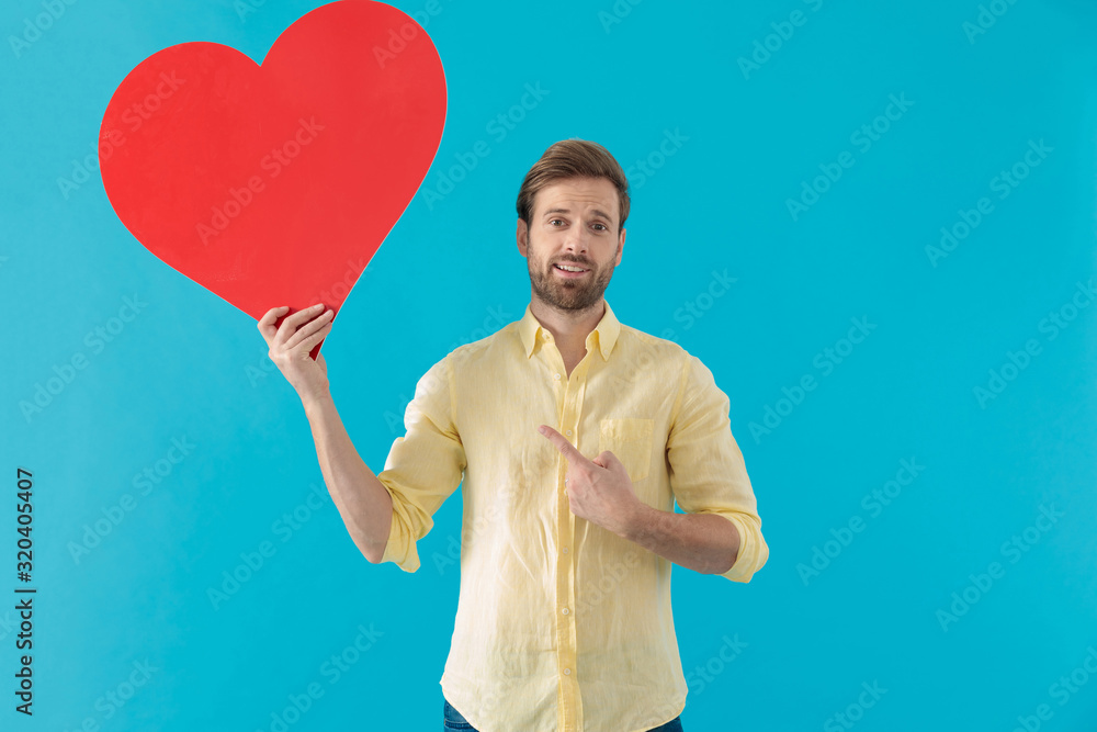 Handsome casual pointing to a heart shape and smiling