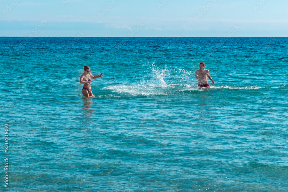 Summer holiday. Happy loving couple are playing splashing sea water.