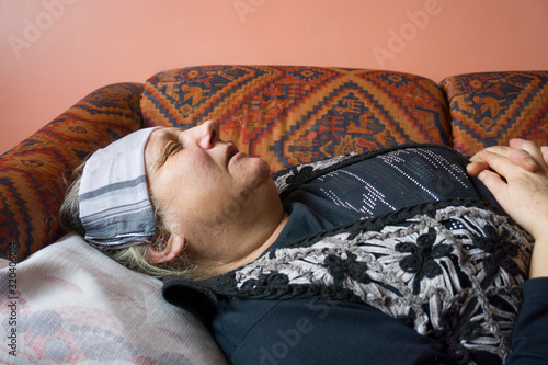 Being febrile. Old woman with headache. Aged woman holding her head and suffering fever heat problem. Elderly senior woman has headache. Unhappy woman in pain lying on sofa at home, feel sick.  photo