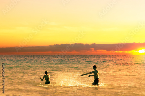 Beach fun couple playing in sea water splashing water at each other at sunset. Summer vacation.