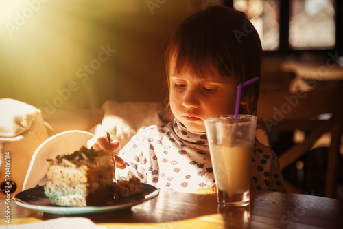 Close up beautiful little child girl eating chocolate cake in a cafe. Food, happiness, joy and positive emotion concept.