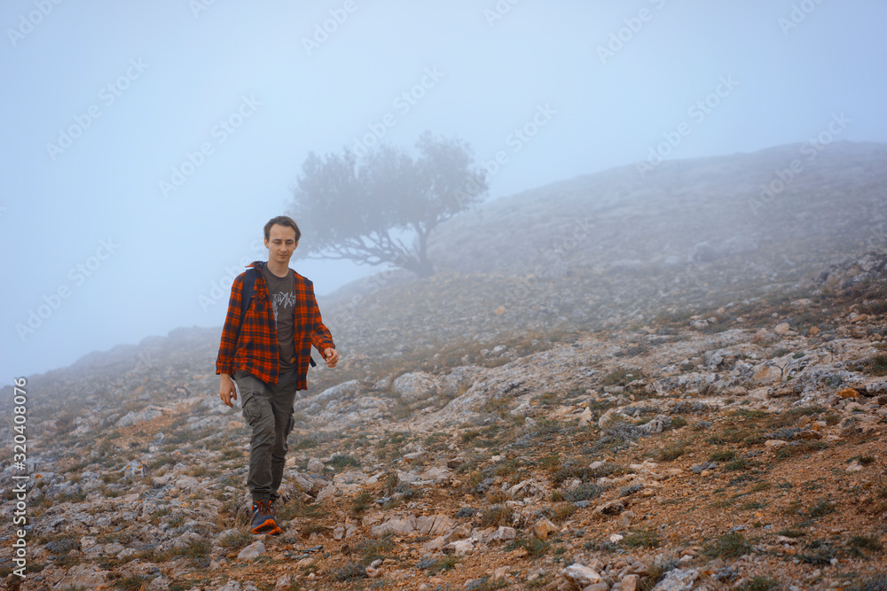 Obraz premium Man in Red Flanel Shirt Hiking in rocky mountains In Thick Fog. Autumn. Tree on Background.