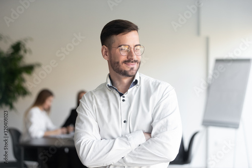 Smiling handsome businessman stands with arms crossed looking away