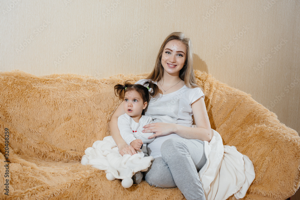 A pregnant mother is sitting on the couch with her little daughter and playing with a gadget A pregnant mother is sitting on the couch with her little daughter and playing with a gadget