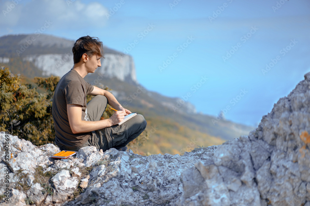 Young Man sitting on rocks and Painting Mountains and sea