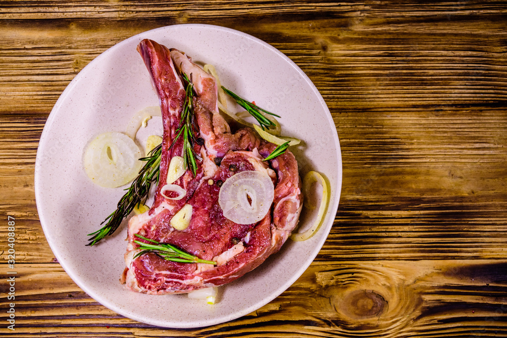 Raw ribeye steak, spices, rosemary, onion and garlic in a ceramic plate on wooden table. Top view Raw ribeye steak, spices, rosemary, onion and garlic in a ceramic plate on wooden table. Top view
