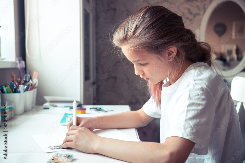 Beautiful pensive girl drawing sketch at her table with light from window 