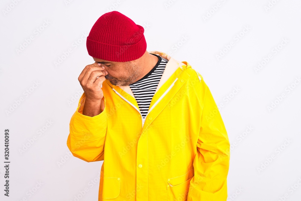 Middle age man wearing rain coat and woolen hat standing over isolated white background tired rubbing nose and eyes feeling fatigue and headache. Stress and frustration concept. Middle age man wearing rain coat and woolen hat standing over isolated white background tired rubbing nose and eyes feeling fatigue and headache. Stress and frustration concept.