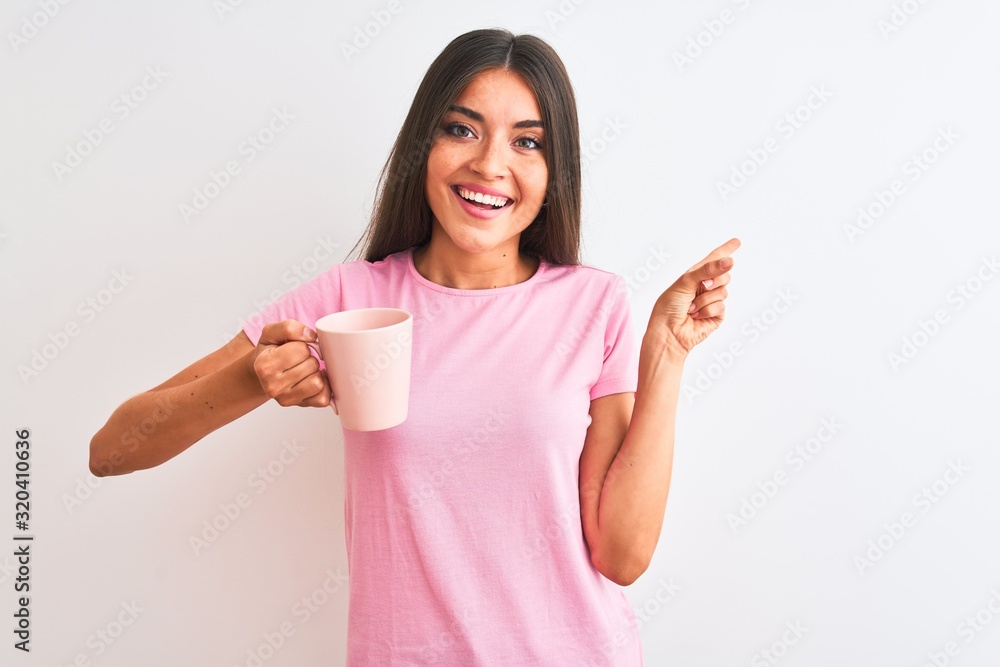 Young beautiful woman drinking pink cup of coffee standing over isolated white background very happy pointing with hand and finger to the side Young beautiful woman drinking pink cup of coffee standing over isolated white background very happy pointing with hand and finger to the side