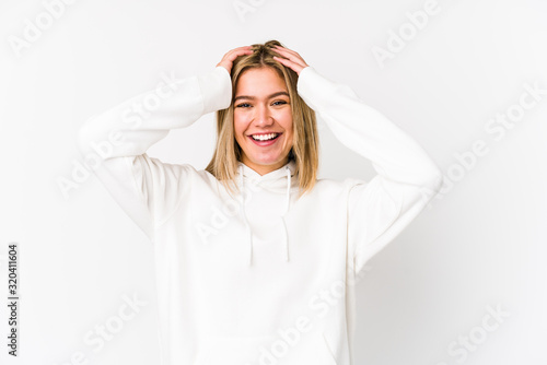 Young blonde caucasian woman isolated laughs joyfully keeping hands on head. Happiness concept.