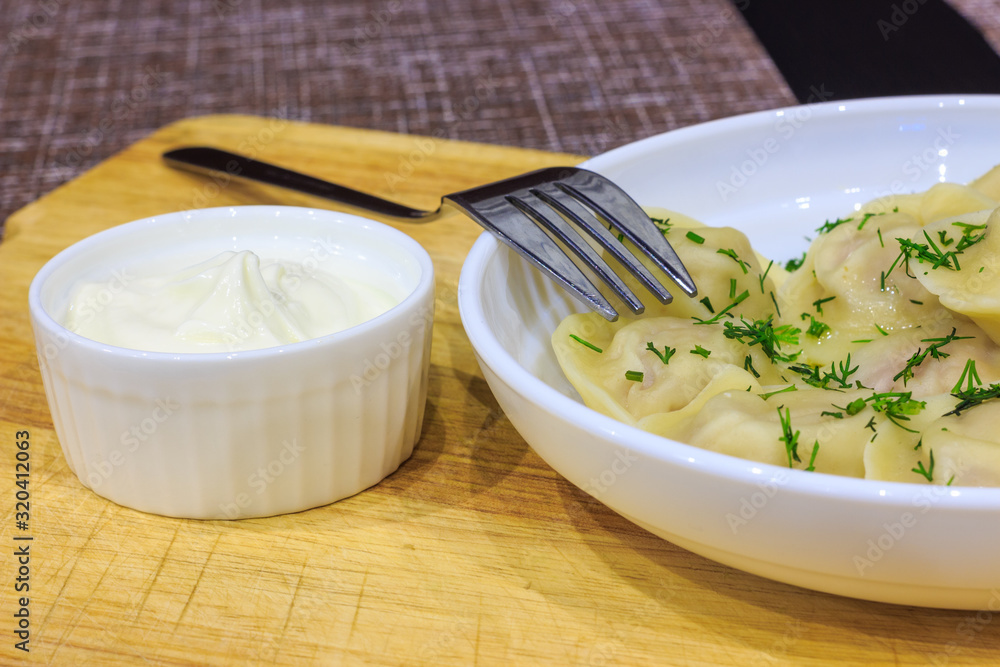 Traditional Russian hand-made dumplings with butter and herbs on a white plate. Traditional Russian hand-made dumplings with butter and herbs on a white plate.