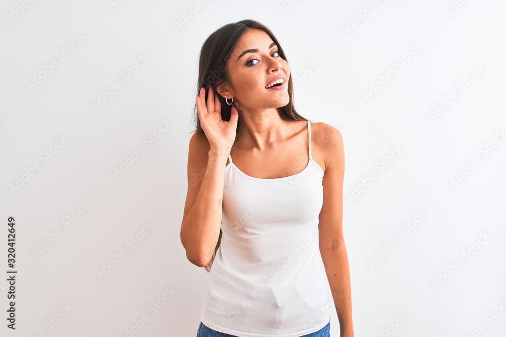 Young beautiful woman wearing casual t-shirt standing over isolated white background smiling with hand over ear listening an hearing to rumor or gossip. Deafness concept. Young beautiful woman wearing casual t-shirt standing over isolated white background smiling with hand over ear listening an hearing to rumor or gossip. Deafness concept.