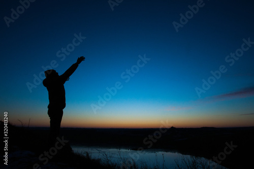 Pray. Silhouetted men on a background of blue sky and sunset. With arms raised. Prayer to God. Glorification. Praising God