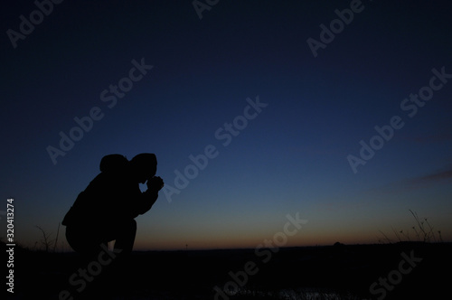 Prayer. Repentance. Silhouetted men on a background of blue sky and sunset. Kneeling Prayer to God. Glorification. Praising God