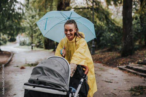 Beautiful and happy middle age woman with her baby walking in city park on rainy day..
