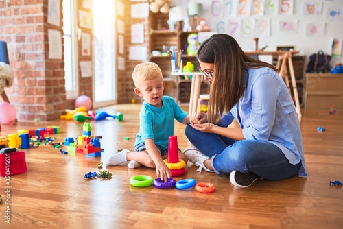 Young caucasian child playing at playschool with teacher. Mother and son at playroom with intelligence toy