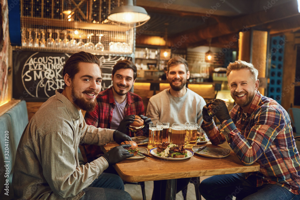 Group of male friends drink beer at a party in a bar. - obrazy, fototapety, plakaty 