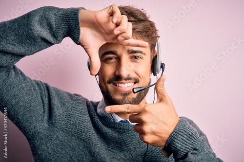 Young call center agent man with beard wearing headset over isolated pink background smiling making frame with hands and fingers with happy face. Creativity and photography concept.