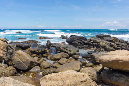 A powerful wave with splashes and foam breaks on a rocky shore. Sri Lanka