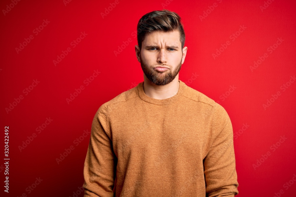 Fototapeta premium Young blond man with beard and blue eyes wearing casual shirt over red background depressed and worry for distress, crying angry and afraid. Sad expression.