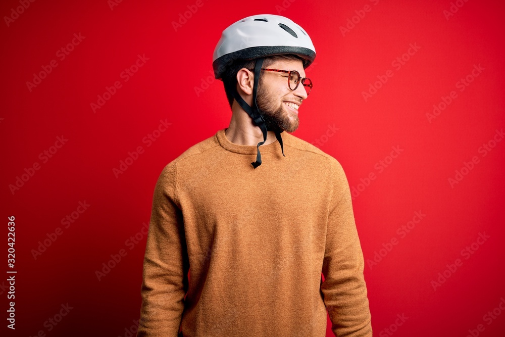 Young blond cyclist man with beard and blue eyes wearing bike helmet and glasses looking away to side with smile on face, natural expression. Laughing confident. Young blond cyclist man with beard and blue eyes wearing bike helmet and glasses looking away to side with smile on face, natural expression. Laughing confident.