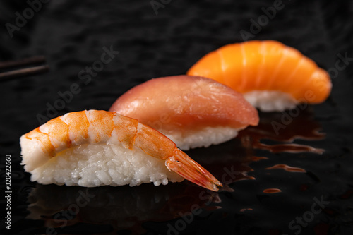 Nigiri sushi set with shrimp, salmon and tuna on black glossy plate, selected focus