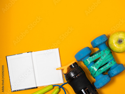 Athlete's set with female clothing, dumbbells and bottle of water on yellow