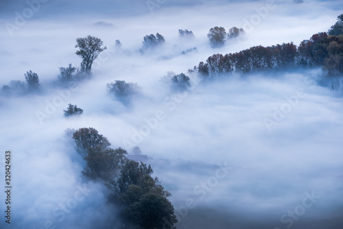 Abstract with Airuno on Adda river in Italy at sunrise with myst fog trees foliage in autumn fall season photo