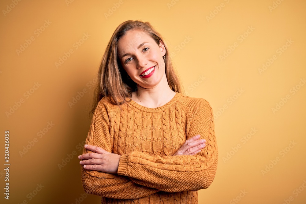 Young beautiful blonde woman wearing casual sweater standing over yellow background happy face smiling with crossed arms looking at the camera. Positive person. Young beautiful blonde woman wearing casual sweater standing over yellow background happy face smiling with crossed arms looking at the camera. Positive person.
