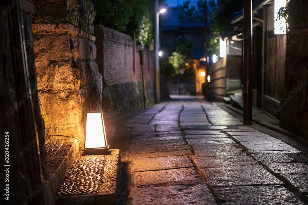Lamps illuminate old stone road through traditional Japanese neighborhood at night