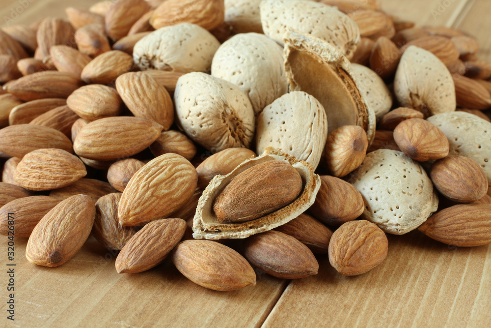 Pile of peeled raw almonds and raw almonds with shells on wooden table. Closeup Pile of peeled raw almonds and raw almonds with shells on wooden table. Closeup