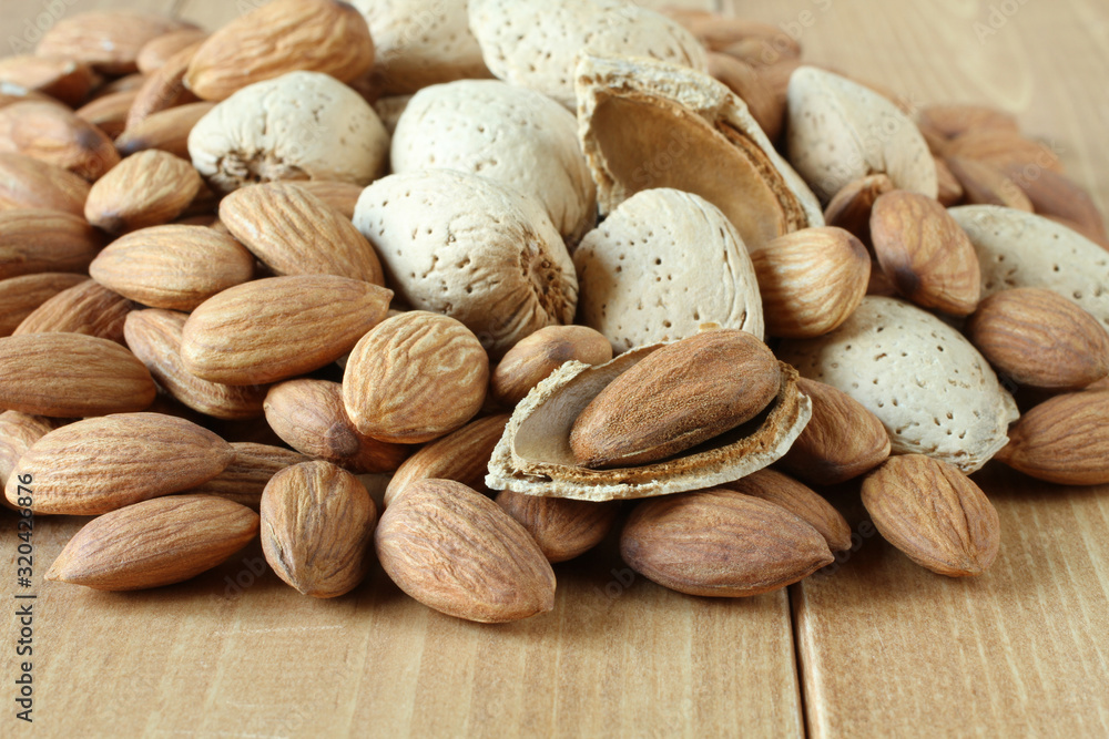 Pile of peeled raw almonds and raw almonds with shells on wooden table. Closeup Pile of peeled raw almonds and raw almonds with shells on wooden table. Closeup