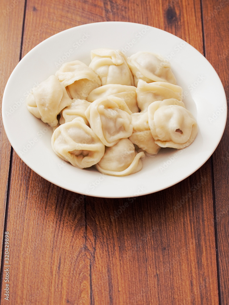 Portion of Russian traditional big size dumpling on a white plate and wooden table. Portion of Russian traditional big size dumpling on a white plate and wooden table.