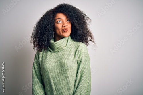 Young beautiful african american woman with afro hair wearing green winter sweater smiling looking to the side and staring away thinking. © Krakenimages.com
