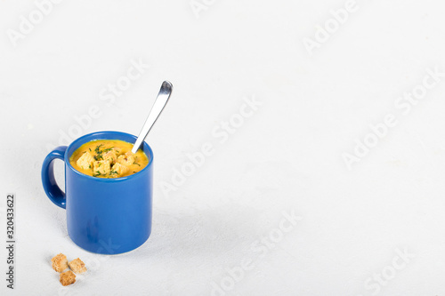 Pumpkin soup-puree with cream, wheat croutons and greens in a blue mug on a light background