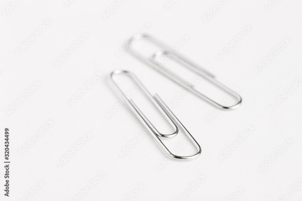 Two silver paper clips close up with shallow depth of field on white surface Two silver paper clips close up with shallow depth of field on white surface
