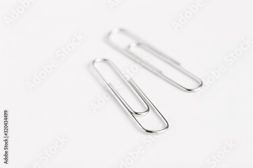 Two silver paper clips close up with shallow depth of field on white surface