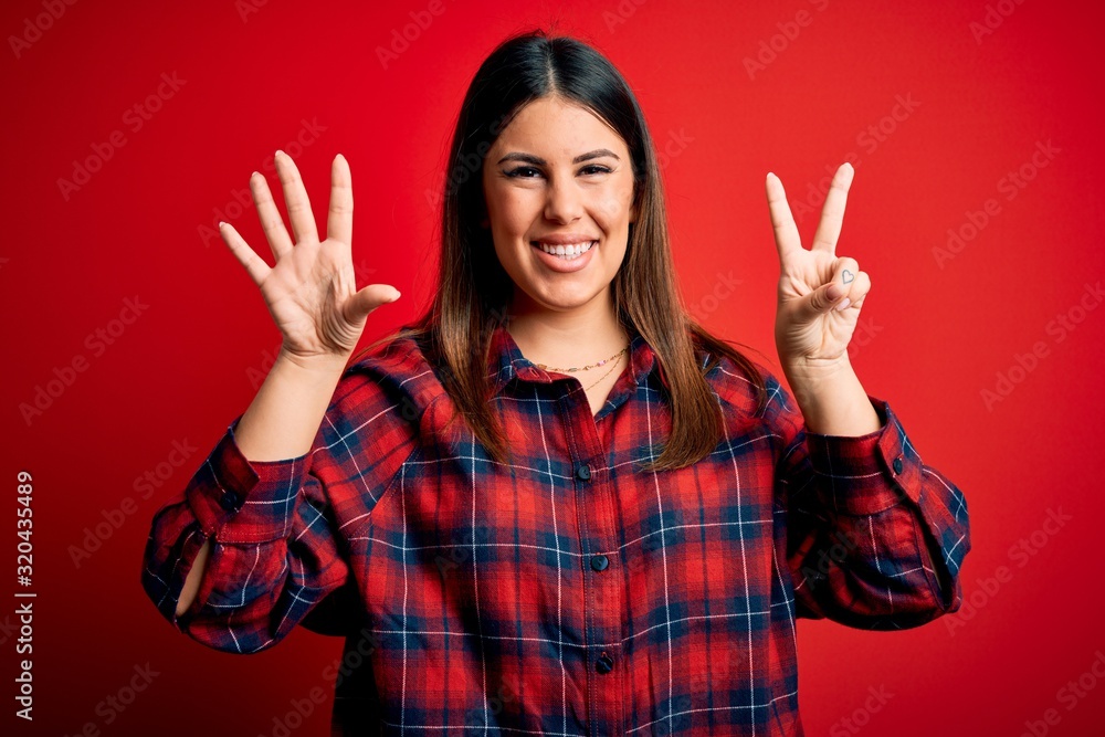 Young beautiful woman wearing casual shirt over red background showing and pointing up with fingers number seven while smiling confident and happy. Young beautiful woman wearing casual shirt over red background showing and pointing up with fingers number seven while smiling confident and happy.